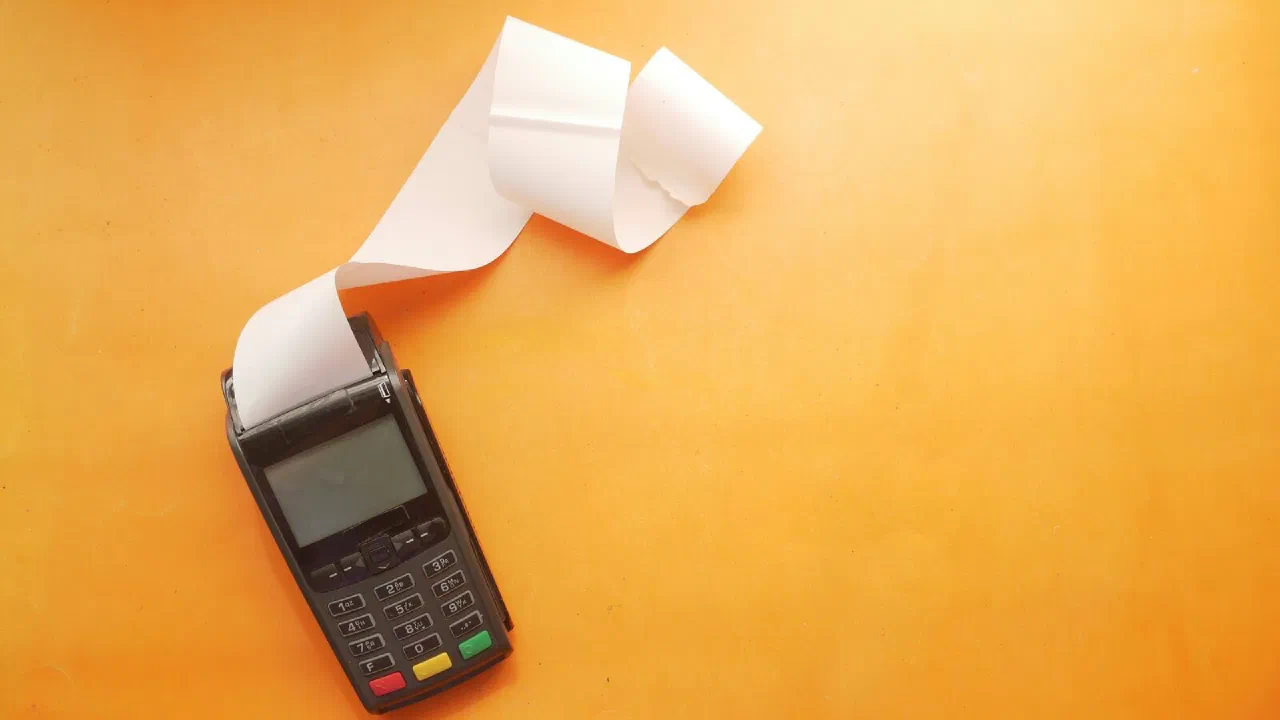 a payment terminal with a long paper receipt against an orange background