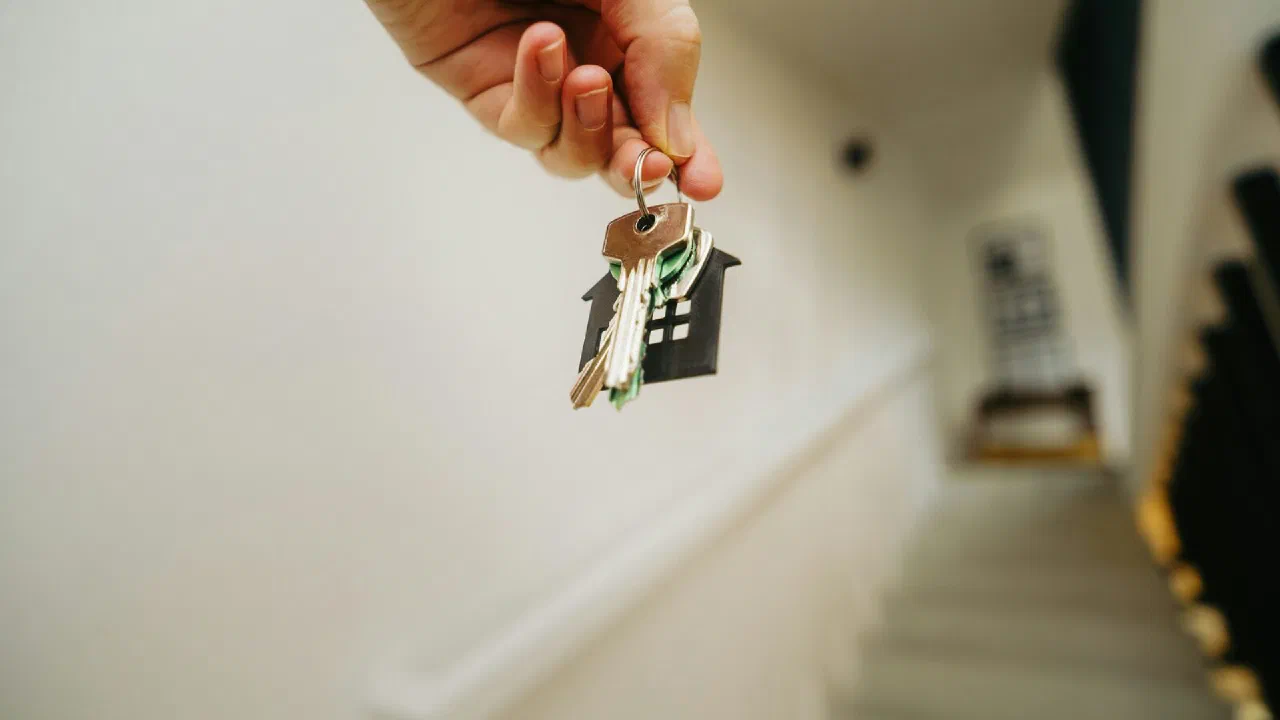 A hand holding a single door key on a stairway landing