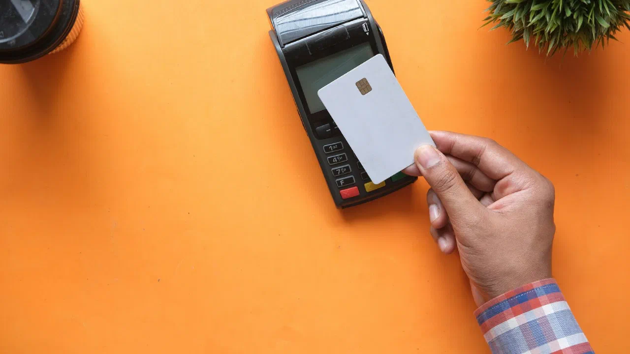 a hand holding a blank payment card beside a card terminal