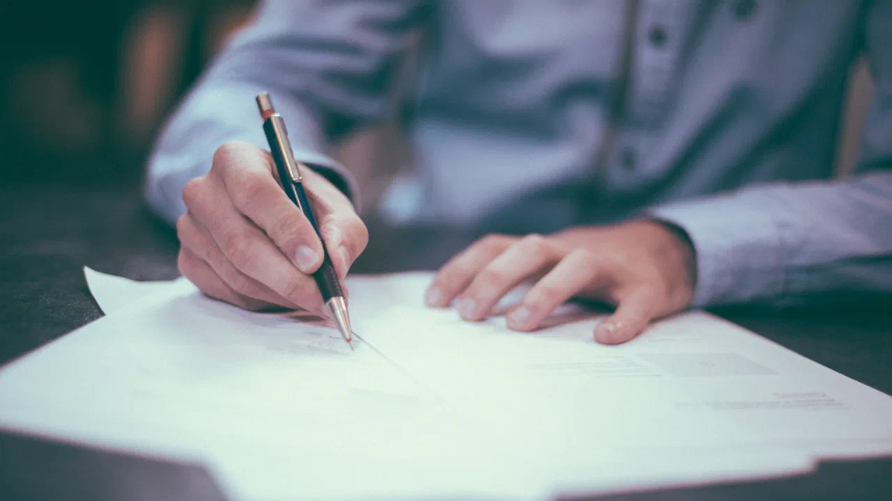 a person signing a printed document with a pen