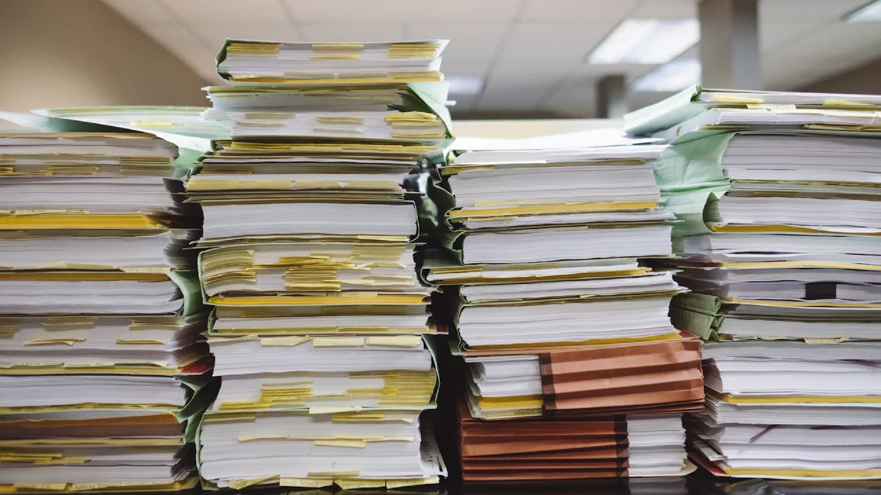 stacks of paper documents and file folders on a desk