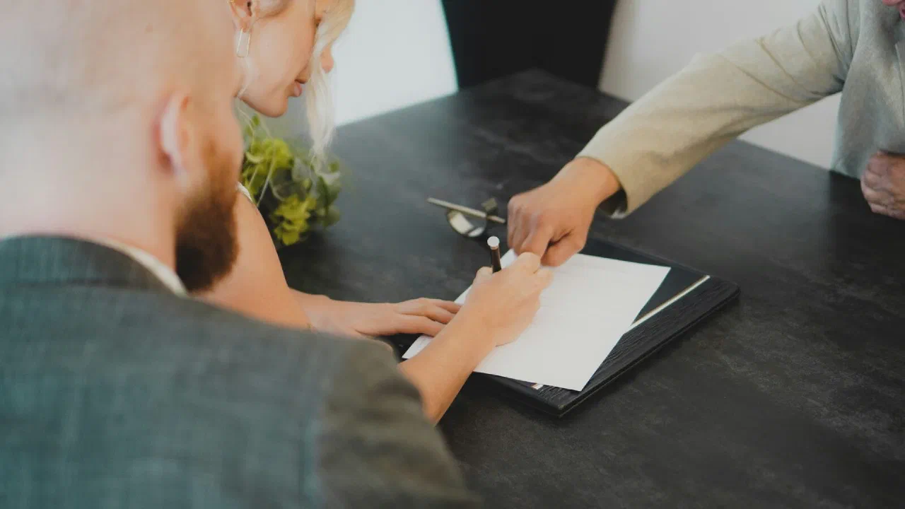 Two people sitting at a desk signing a printed document