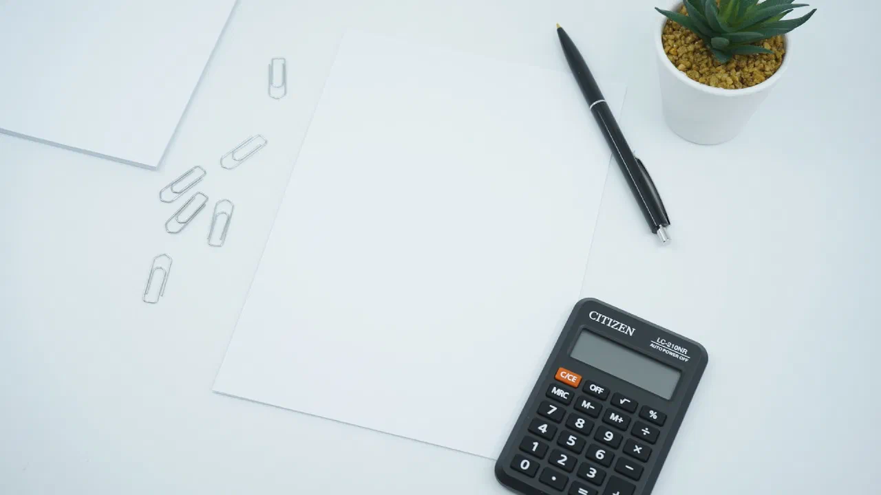 a calculator and a pen beside a blank sheet of paper on a desk